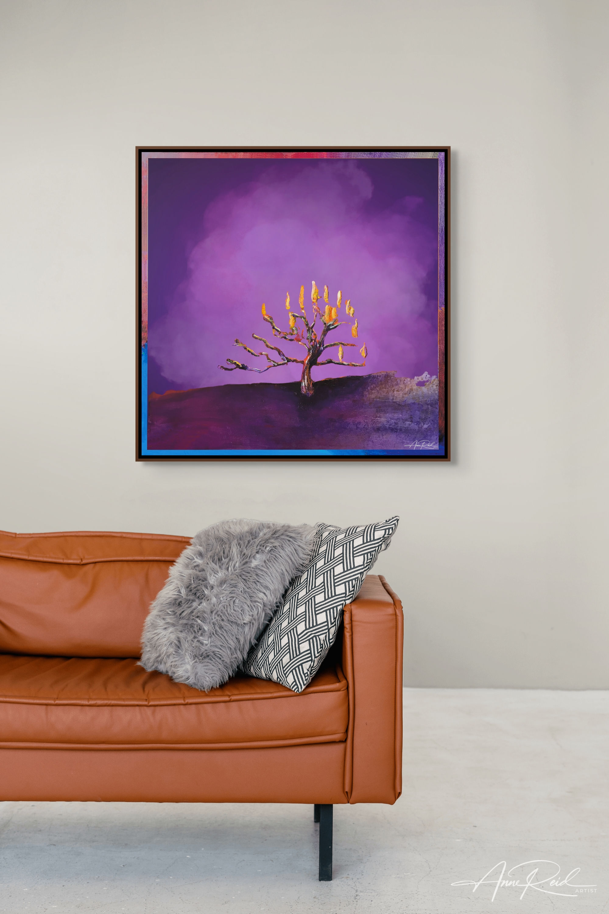 Framed abstract tree on fire painting with vivid purples above leather sofa