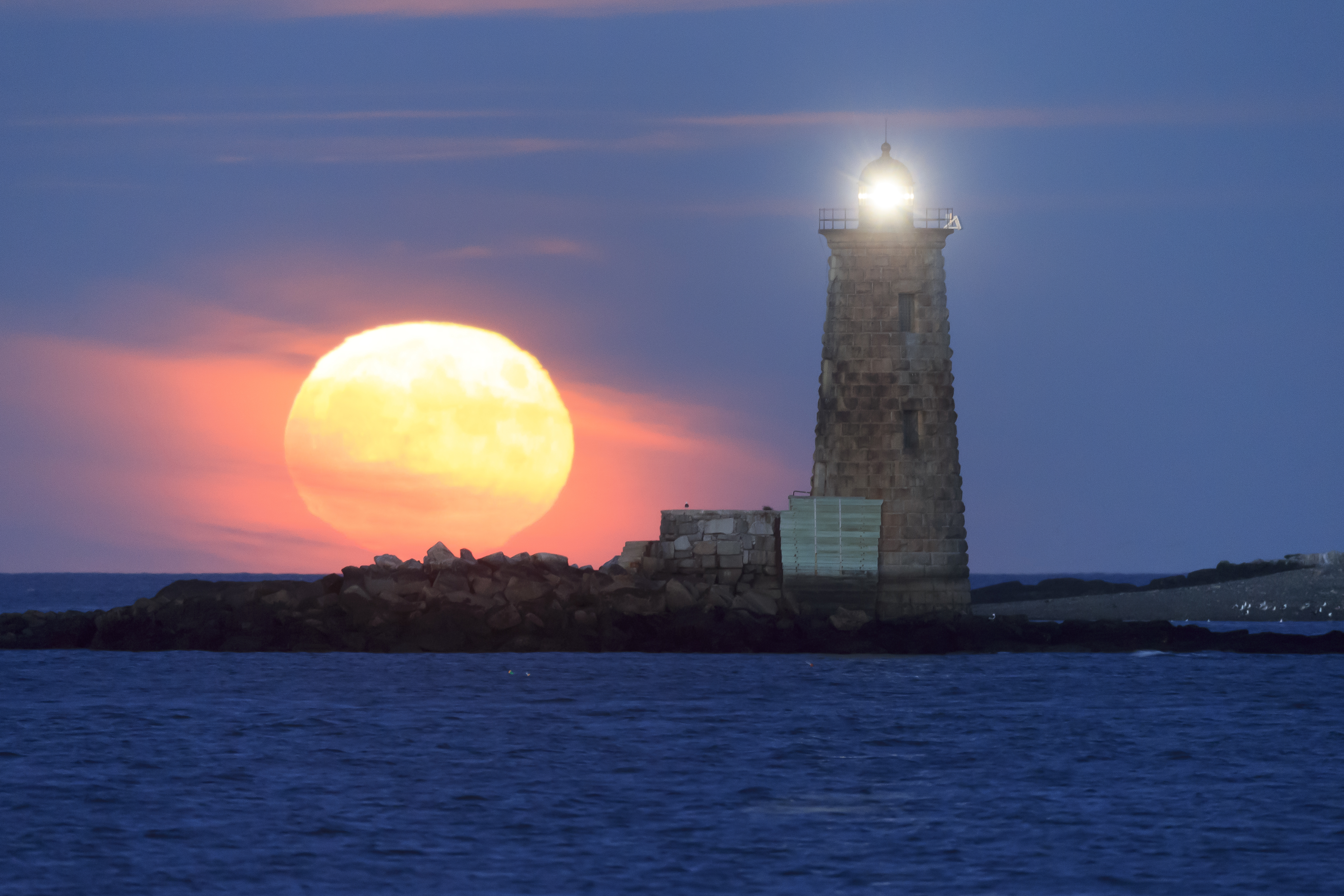 Coastal lighthouse at blue hour with reflective water—reading moon phase, tide state, and wind for surface light.