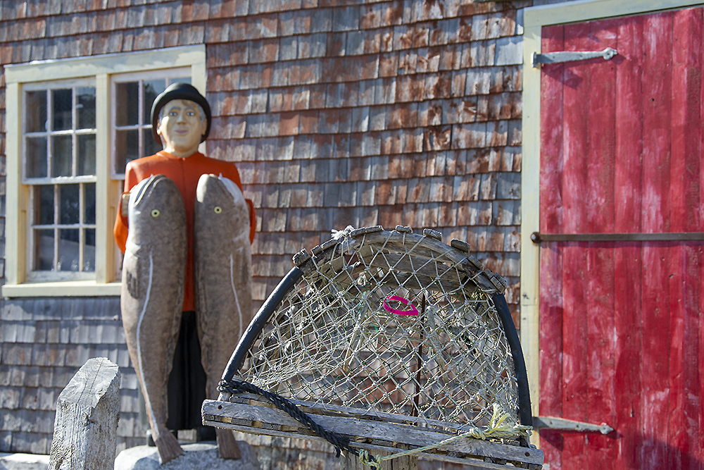 Traditional fishing scene at Peggy’s Cove with rustic statue, lobster traps, and weathered coastal building