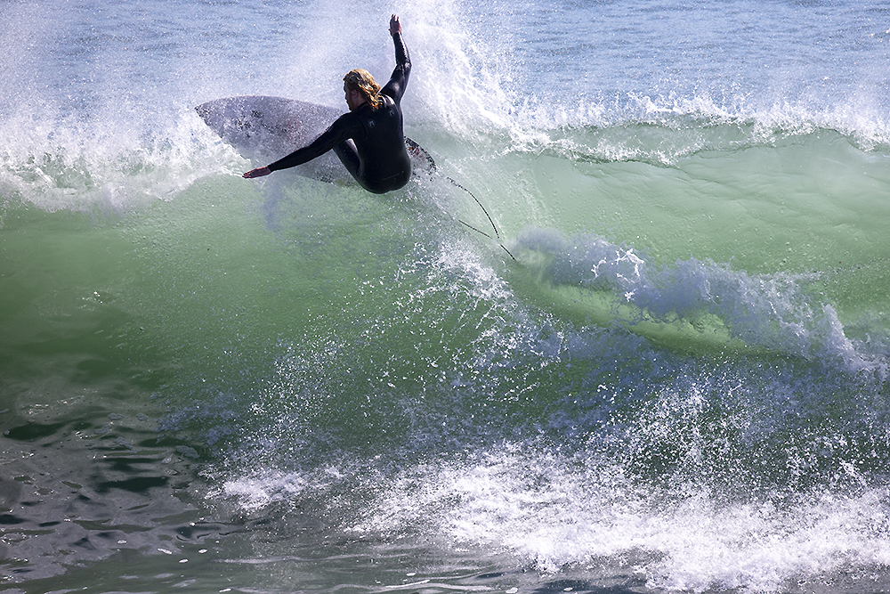 A surfer carving through a powerful ocean wave, symbolizing the boundless, interconnected journey of a hydrogen qubit, free from linear constraints and moving through a vast, quantum field of infinite possibilities.