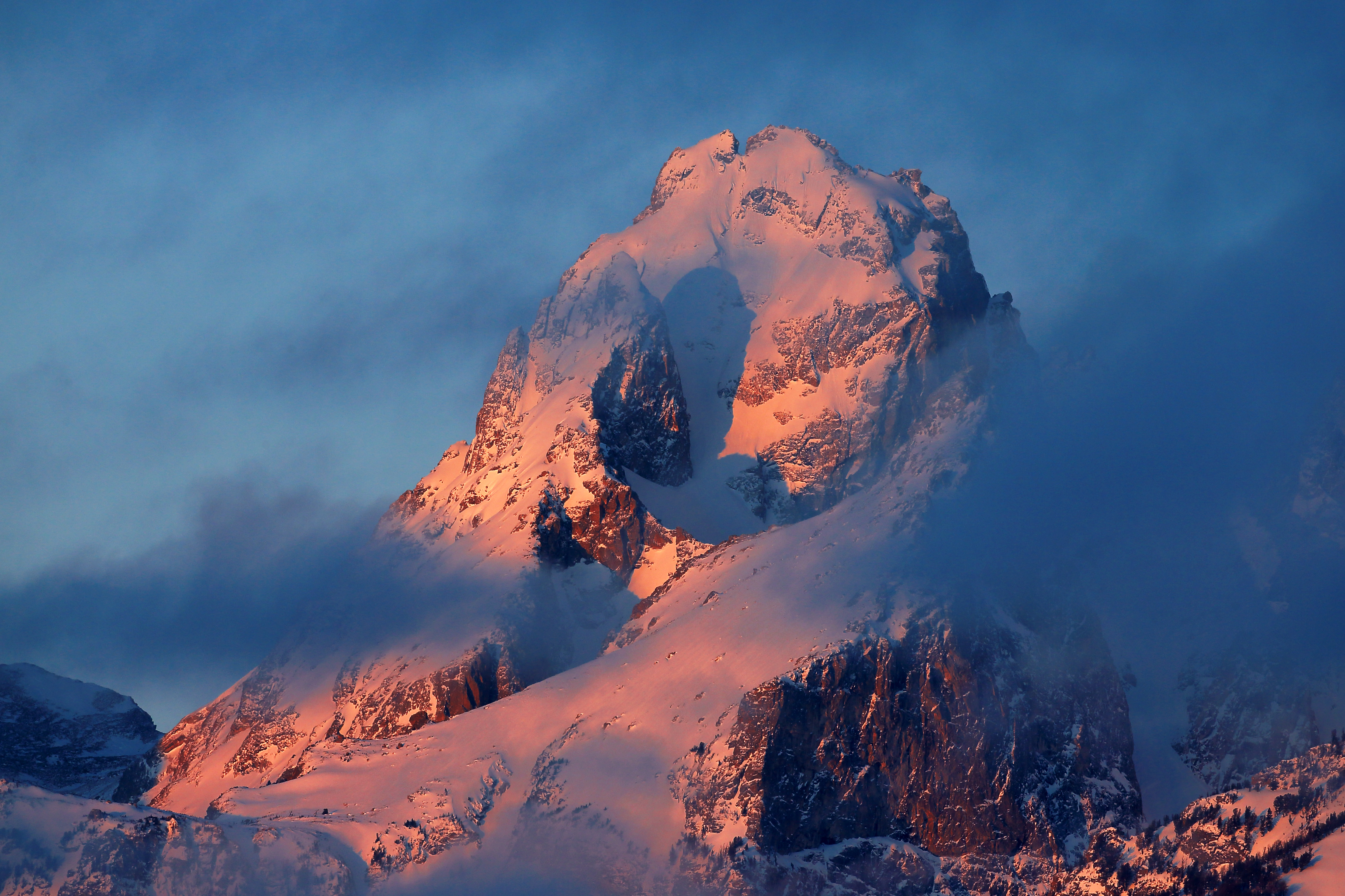 Alpenglow illuminating a towering snow-covered mountain peak above drifting clouds