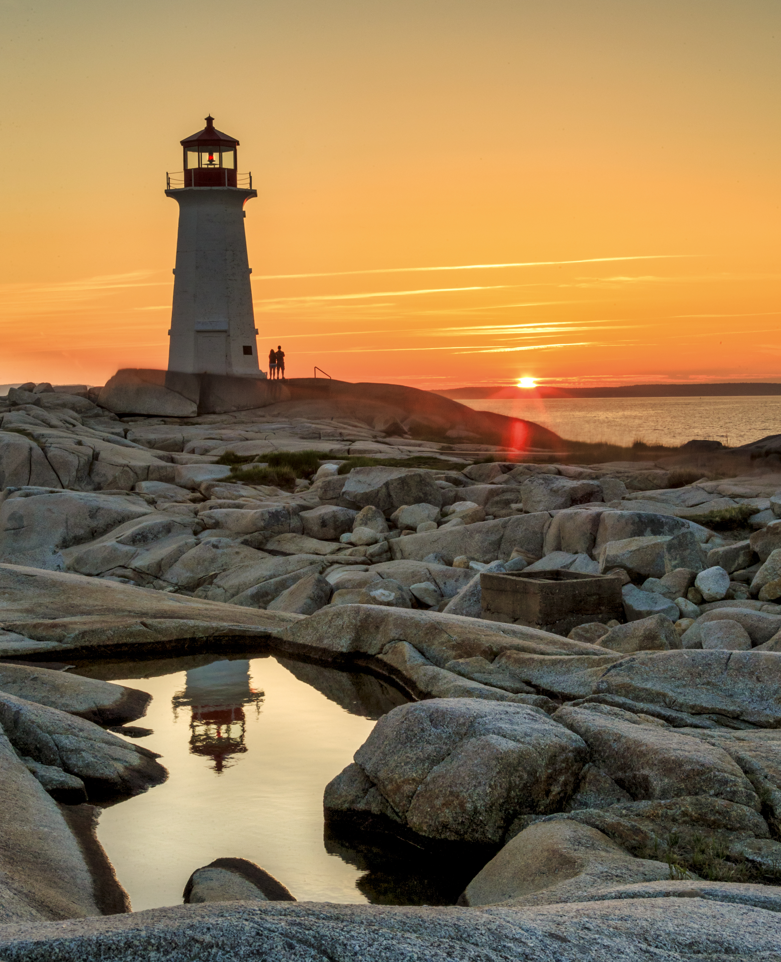 Sunrise over Peggy's Cove lighthouse, illuminating granite cliffs with warm golden light along the Atlantic coast of Nova Scotia