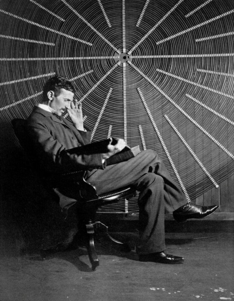 Nikola Tesla seated in front of a massive spiral coil, reading a book in contemplative posture.