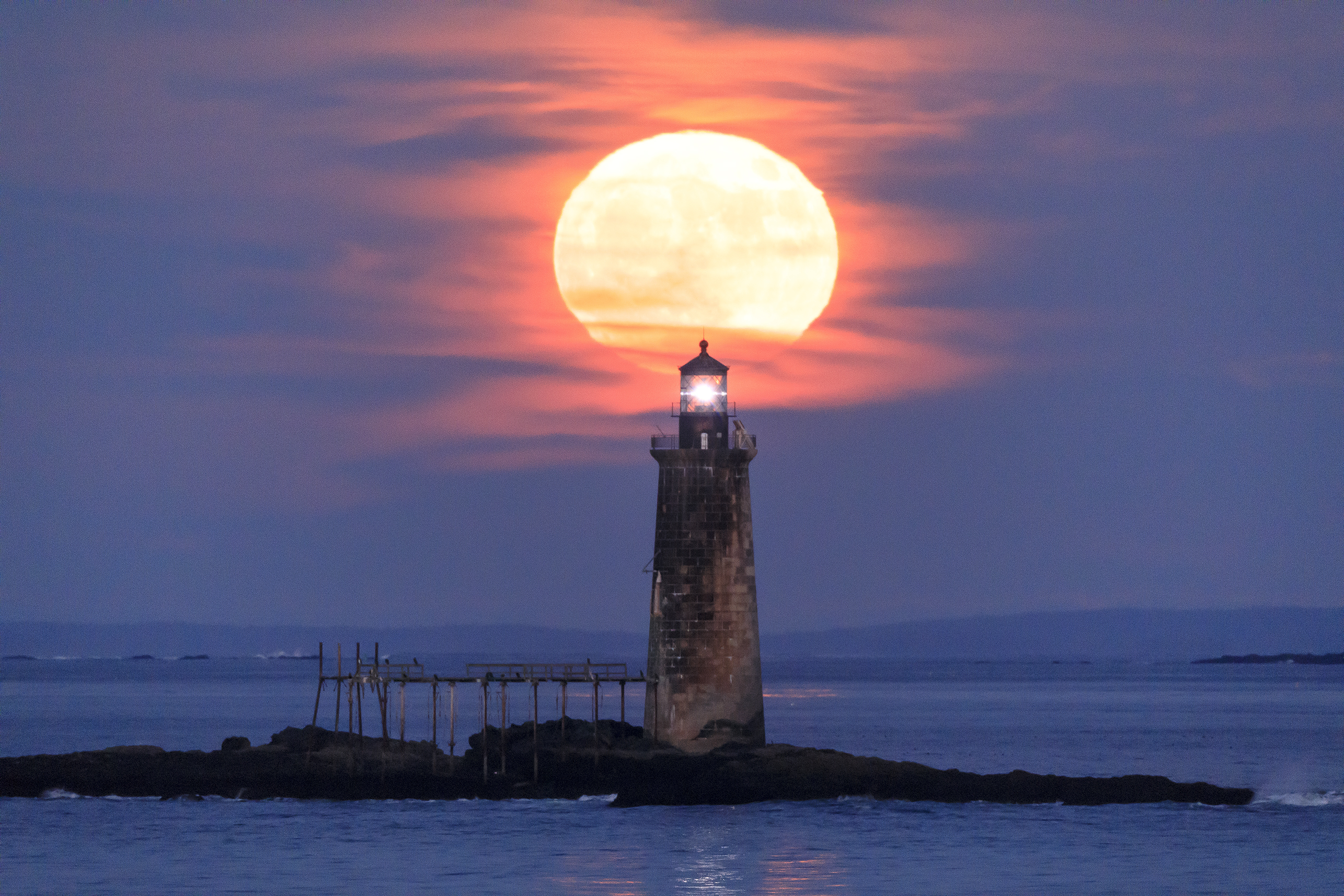 Lighthouse standing over a calm sea at dusk with soft tidal reflections