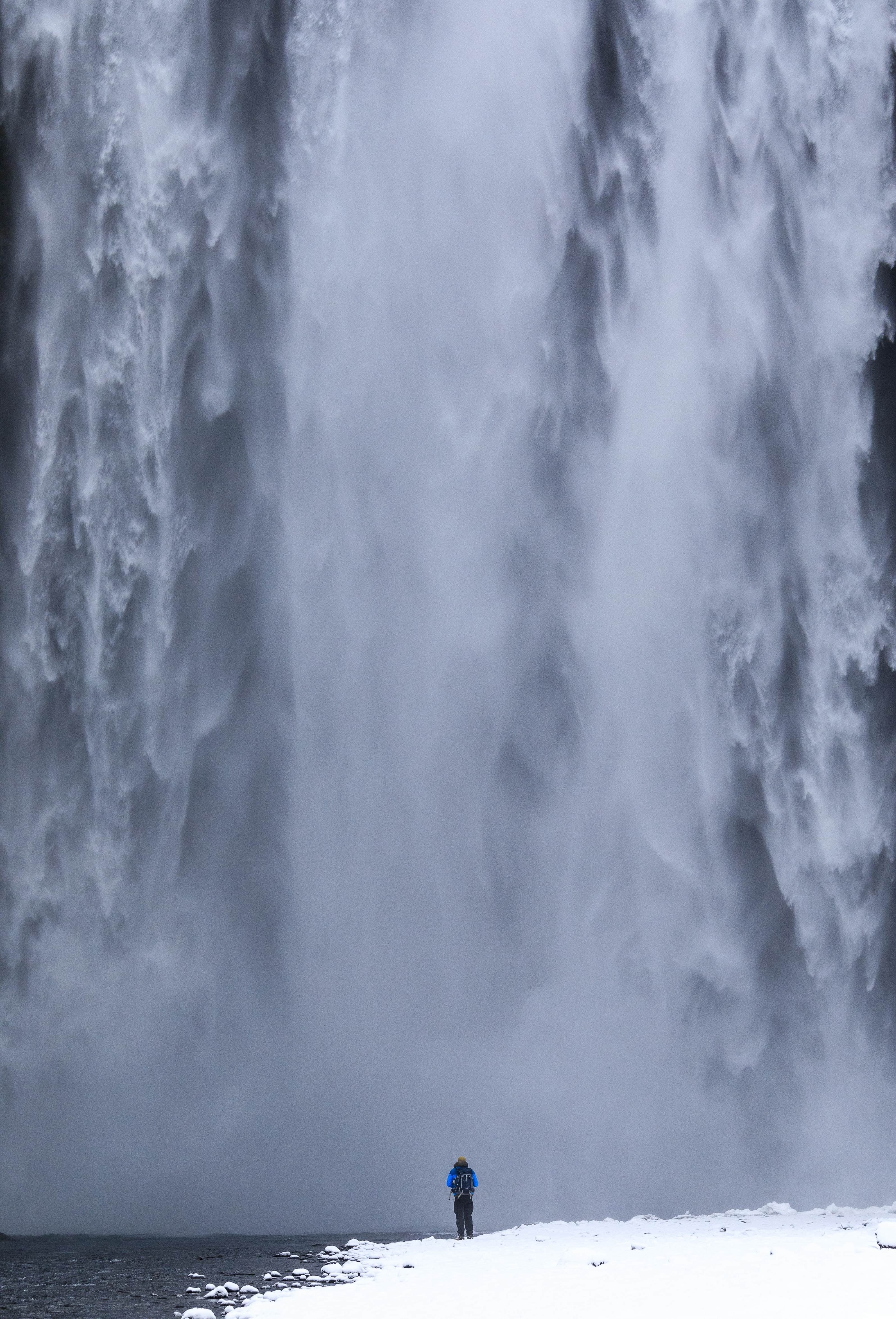 A lone hiker standing at the base of a massive cascading waterfall, symbolizing the awe-inspiring potential of harnessing natural elements like hydrogen for sustainable innovation.