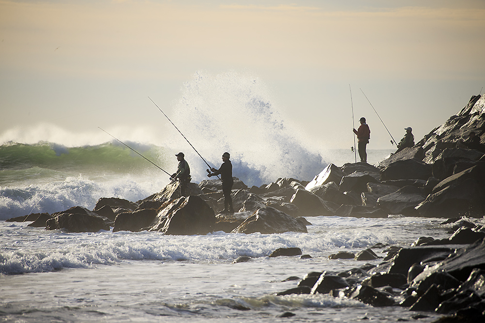 Fishermen standing along the rocky shoreline at Montauk Point as waves break and ocean energy builds during migration season