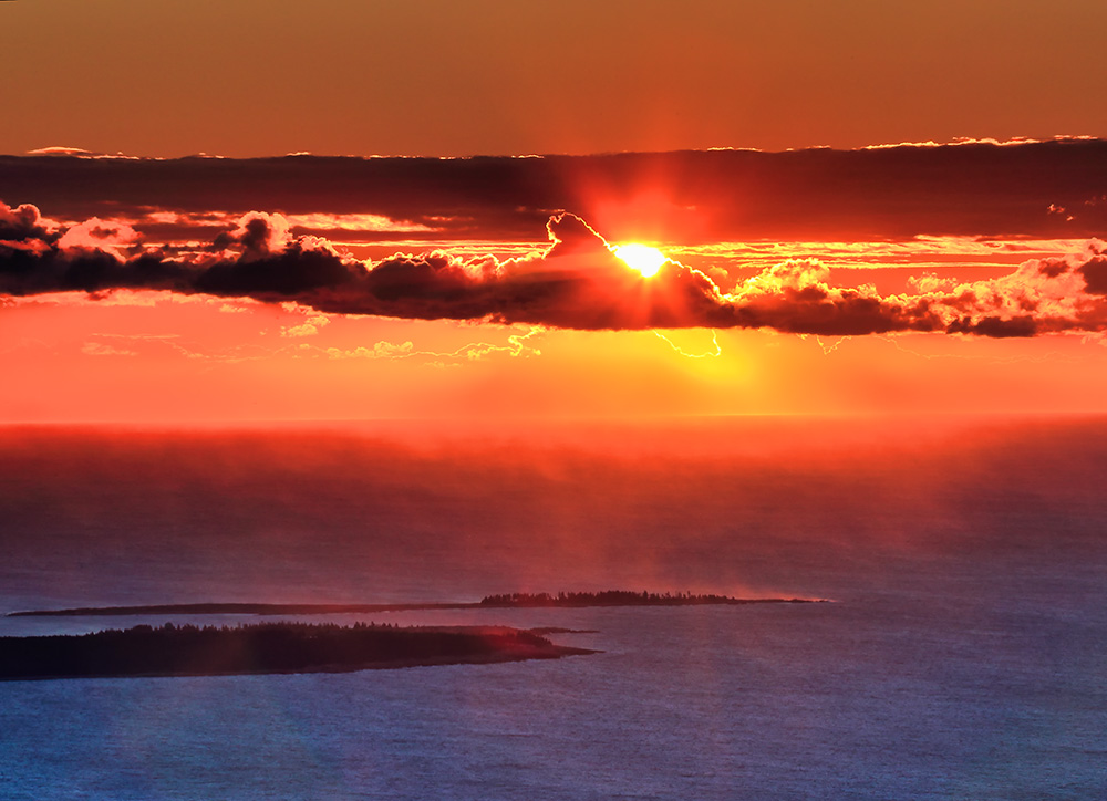 Golden sunrise light spreading across Cadillac Mountain granite and Atlantic coastline in layered sequence