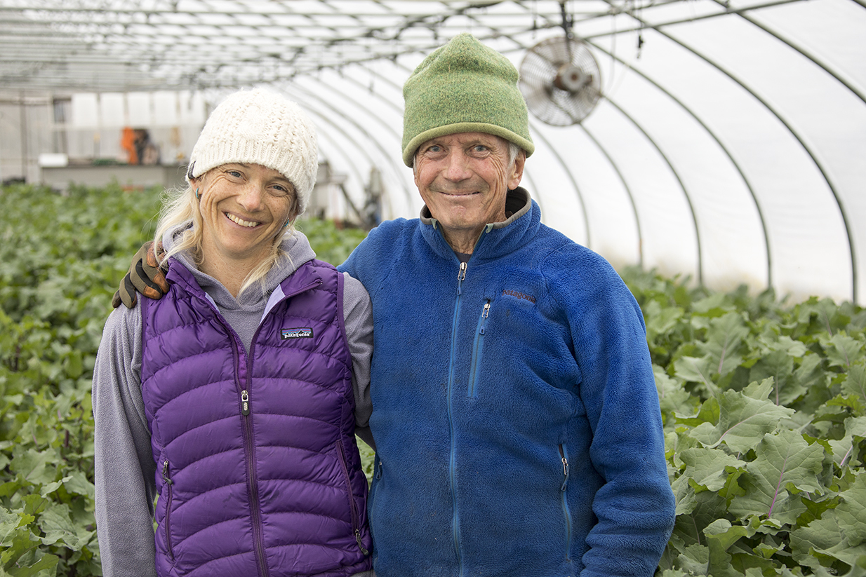 Eliot Coleman and Clara Coleman standing together inside a bright greenhouse at Four Season Farm