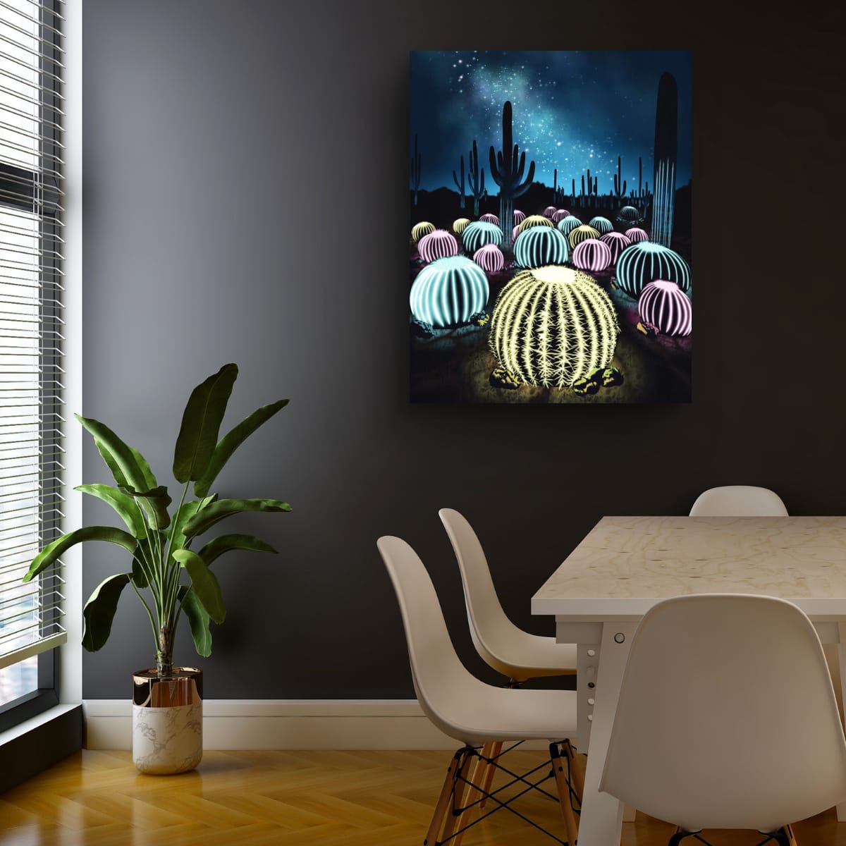 Neon desert wall art featuring glowing barrel cacti under a star-filled night sky displayed above a white dining table in a modern room with dark charcoal walls, white chairs, wood flooring, and a potted green plant by the window.